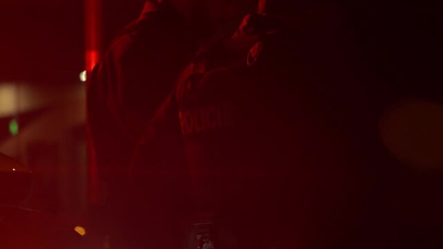 Police officer standing by a patrol car with flashing blue emergency lights at night. Cinematic law enforcement scene with dramatic lighting, lens flares, and tactical atmosphere.