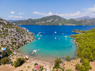 Sig Liman Bay in Selimiye, Marmaris, Mugla, Türkiye, features turquoise waters, anchored boats, and a lively beach surrounded by forested hills and Mediterranean scenery. © osmanmaasoglu