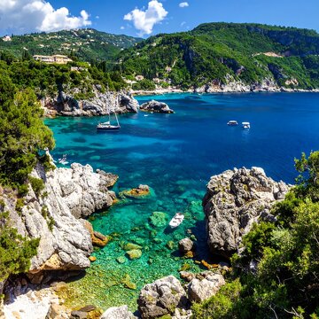 A picturesque seaside scene showcases vibrant turquoise waters embracing rocky cliffs and lush green hills, with a yacht and boats scattered