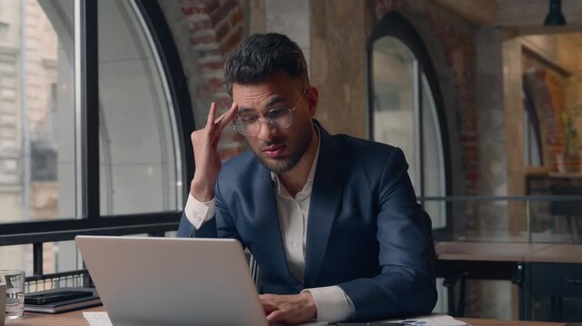 Indian businessman Arabian business man with laptop feeling headache pain thinking difficult task computer problem Hispanic male guy entrepreneur frustrated in office overworked tired feel migraine