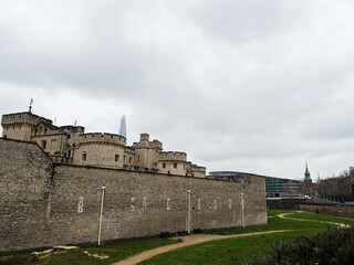 Fototapeta premium Tower of London castle and medieval stone walls beside modern city skyline in London, UK on an overcast day