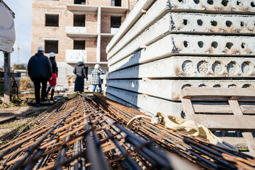Naklejka premium Workers walk past stacks of concrete blocks and steel rods at a new building site under bright sunlight