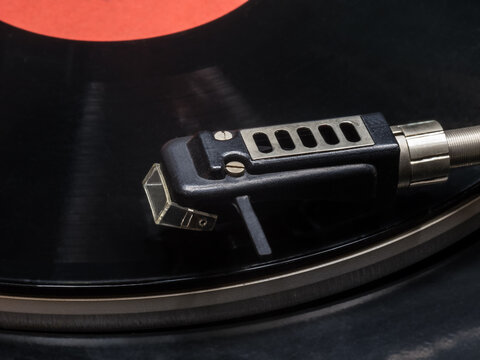 A headshell with an electromagnetic head of a vinyl record player mounted on it against the background of a gramophone record.