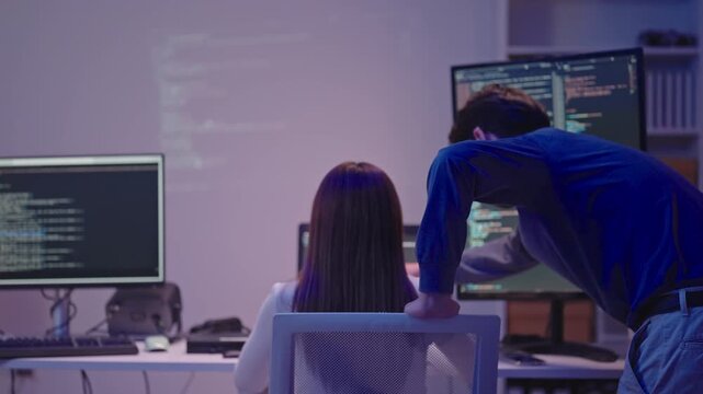 Professional male and female programmers discussing software architecture and coding in a dark office.