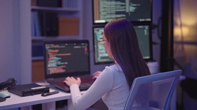 Focused female software engineer working on a programming project at her desk late at night.