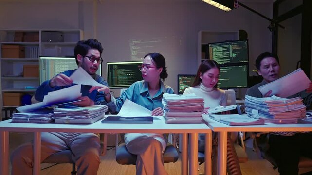 Group of Asian colleagues pan shot searching through disorganized piles of documents, feeling rushed and stressed to meet a night deadline.
