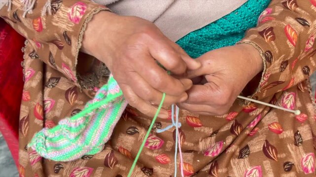 Elderly female hand knitting from wool. Knitting sweater with wrinkly hands. Colorful Crochet with old hands. close-up hands knitting sweater. House wife knitting in free time. Old lady knitting 