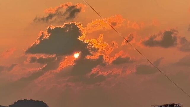 Parasailing activity over the sea at sunset on Phuket island, Thailand. Tourist flying with colorful parachute above the ocean with boats and jet skis on the shore during golden hour.
