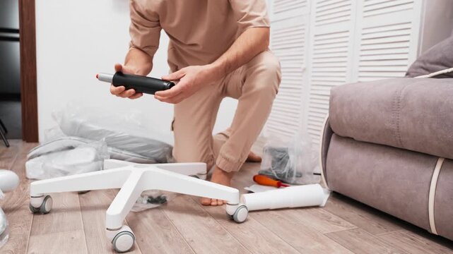 Man assembling office chair at home using tools. DIY furniture setup process in modern interior. Concept of home improvement, manual work, and comfortable workspace preparation.