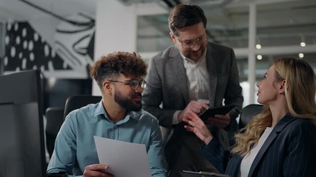 Three multiracial business managers working discussing documents statistic data reviewing papers talking multiethnic diversity businessmen men businesswoman woman talk using digital tablet in office