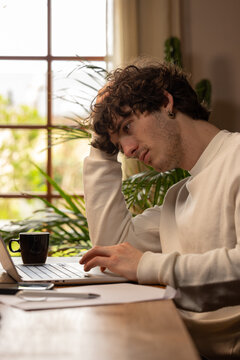 Jeune homme en situation de stress face &agrave; son ordinateur, illustrant la pression du t&eacute;l&eacute;travail et la fatigue mentale dans un environnement domestique lumineux.