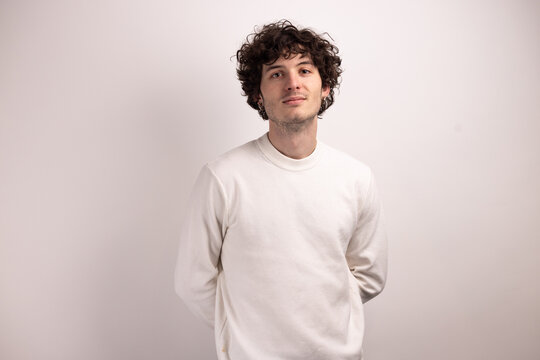 Portrait d&rsquo;un beau jeune homme de 20 ans aux cheveux boucl&eacute;s souriant sur fond blanc, exprimant confiance, naturel et simplicit&eacute; dans un style minimaliste