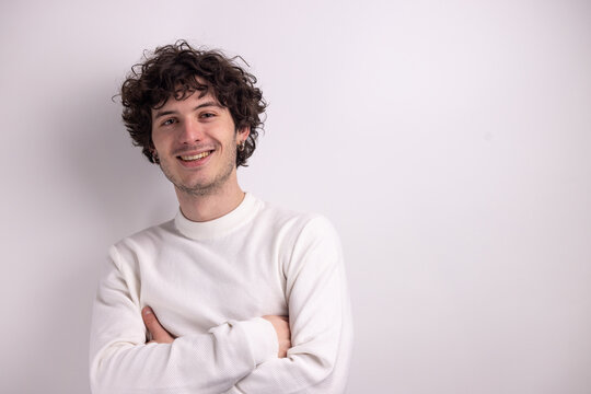Portrait d&rsquo;un beau jeune homme de 20 ans aux cheveux boucl&eacute;s souriant sur fond blanc, exprimant confiance, naturel et simplicit&eacute; dans un style minimaliste