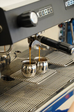 Double shot of espresso pouring from coffee maker into small steel jugs