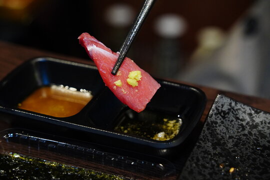 close-up photo of a piece of fresh tuna sashimi picked up with chopsticks.