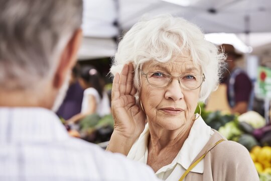 Senior woman with glasses straining to hear a man at a market.