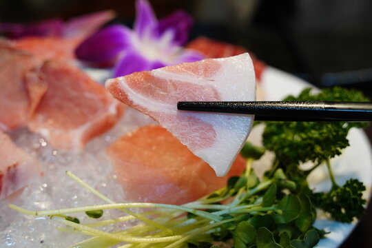 close-up photo of a piece of fresh tuna sashimi picked up with chopsticks.