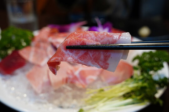 close-up photo of a piece of fresh tuna sashimi picked up with chopsticks.