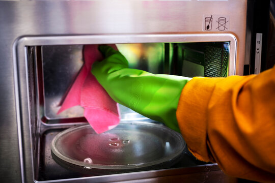 Woman cleaner wipes inside of microwave oven with pink cloth. Kitchen appliance maintenance and professional cleaning service.