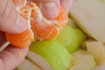 Closeup photo of man preparing vegan fruit salad. Close-up of hands peeling tangerine over fruit salad preparation