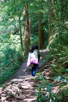 A mother and daughter walking on a dirt trail with exposed roots in a forest