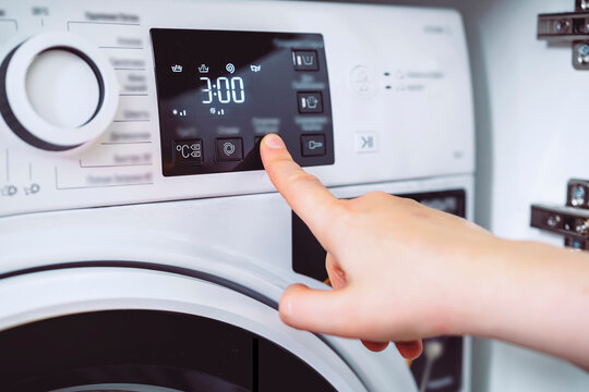 Woman choosing three hour delayed start on washing machine panel. Household task automation for modern busy lifestyle.
