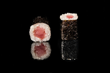 Two tuna maki sushi rolls with nori seaweed and white rice, one showing cross section with fresh raw tuna filling, isolated on black background with mirror reflection. Part of sushi roll series, studi © Vitaliy