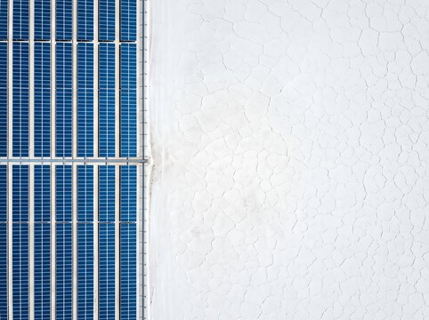 Aerial shot showing a line of solar panels next to a cracked, dry white surface.