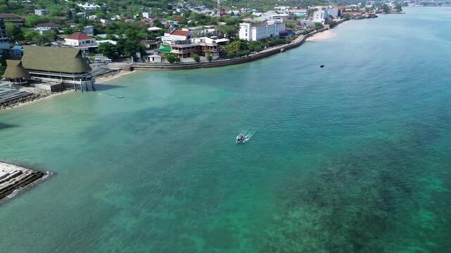 Aerial view of coastal town with thatched roofs and boat on clear water