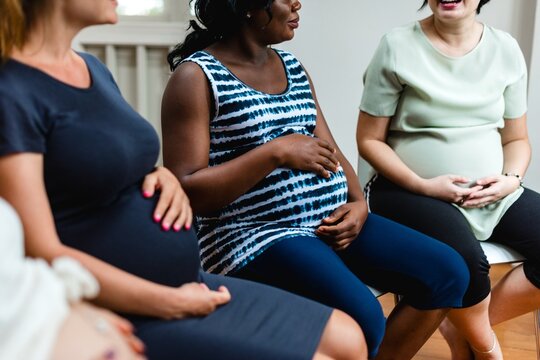 Group of diverse pregnant women sitting together, sharing experiences. Expectant mothers, diverse ethnicities, pregnancy support, prenatal group discussion. Pregnancy and maternity image.