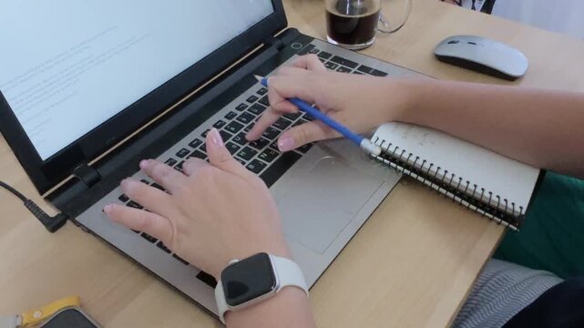 A modern desk setup with hands writing in a notebook, laptop, smartphone, and smartwatch.