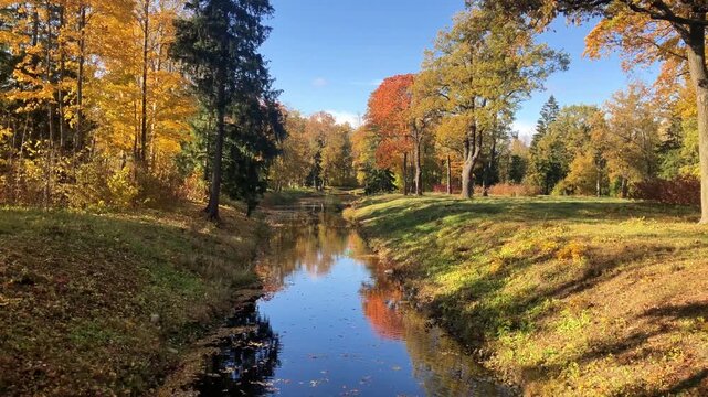 View from a bridge over Vittolovskaya channel in Alexander Park of Tsarskoye Selo, Pushkin, Saint Petersburg, Russia, with colorful autumn trees reflected in water on a sunny day, 4K 60fps