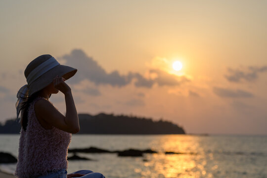 夕焼けの海を見つめる帽子を被った日本人女性
