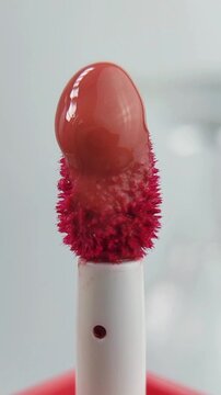 Lip tint liquid melting or dripping on the tip of a brush applicator. Isolated on clean white background, close up view, makeup product concept with glossy texture.