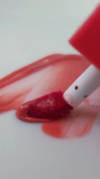 Applying and spreading red lip tint on a white background in a zigzag motion using a brush. Abstract makeup art, bold color strokes, creative cosmetic concept.