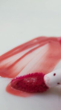 Vertical composition of a white background surface smeared with red or pink lip tint. Abstract cosmetic art, bold pigment stains, creative beauty concept with brush strokes.