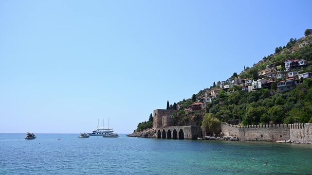 Ancient Seljuk Shipyard (Tersane) and castle walls in Alanya, Turkey. Historical fortress on Mediterranean coast. Yachts in blue harbor. Travel, heritage and summer vacation concept