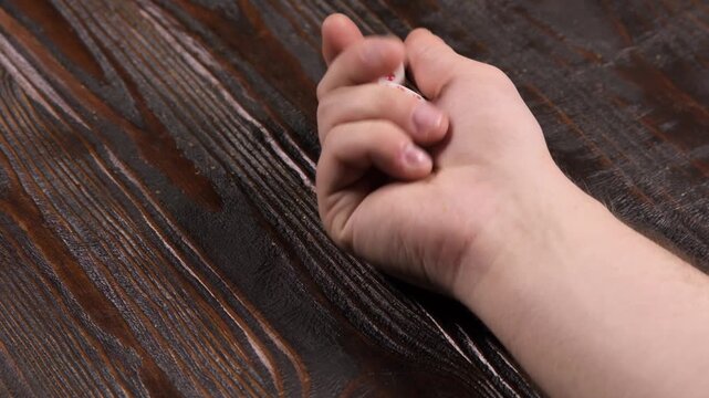 A hand stirs white dice against a wooden table in the daytime, close-up