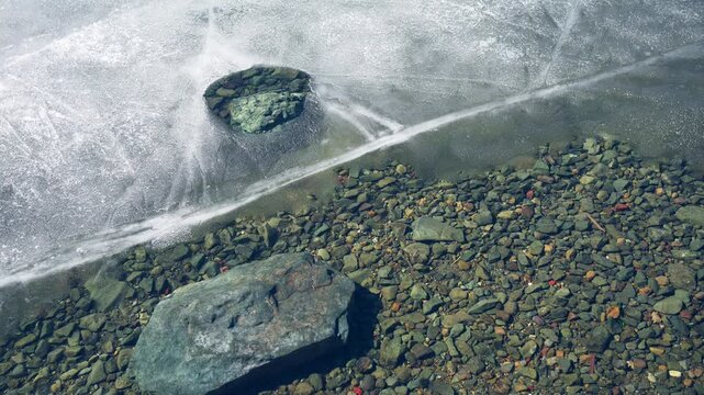 Melting ice on the shore of lake in early spring. Ice floes floating on the water. Colorful stones on the bottom of lake. Beautiful spring nature
