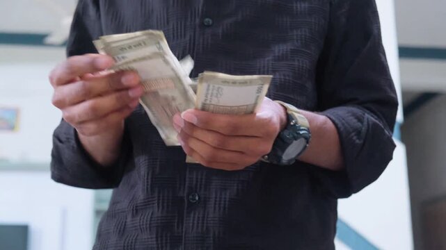 Man in black shirt counting a stack of 500 rupee Indian currency notes