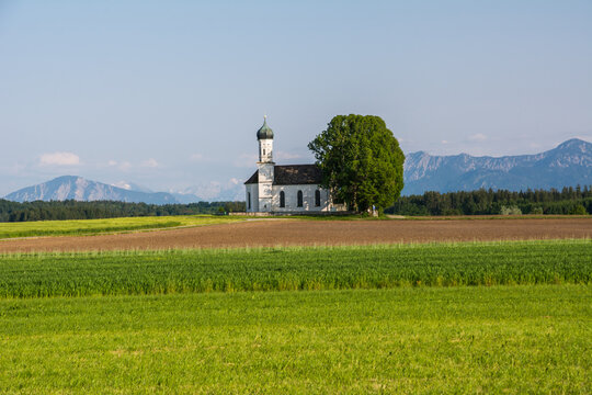 Traditional Bavarian chapel St. Andreas in Etting with a panoramic view of the Alps and green fields
