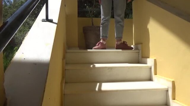 Girl in sneakers on stairs making leg movements and steps to music
Lower part of person in blue pants and pink sneakers moving to music and making steps while dancing on stairs