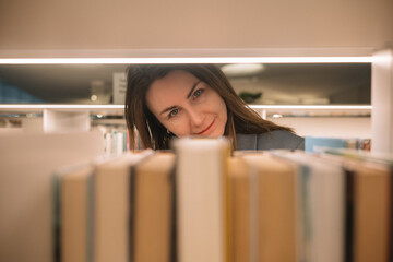 Woman looking through bookshelves in a library during daytime while browsing for reading material © Irina Magrelo