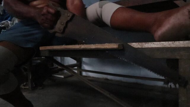 a Javanese man is sawing a wooden board