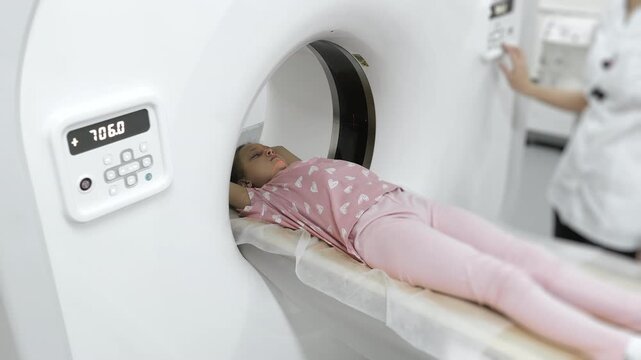 Medical worker adjusting CT scanner while child patient lies on table during diagnostic imaging procedure in hospital.