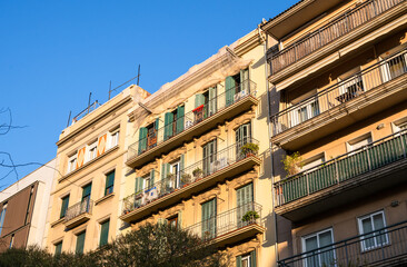 Fototapeta premium Sunlit residential building facade with balconies and green shutters in Barcelona urban architecture