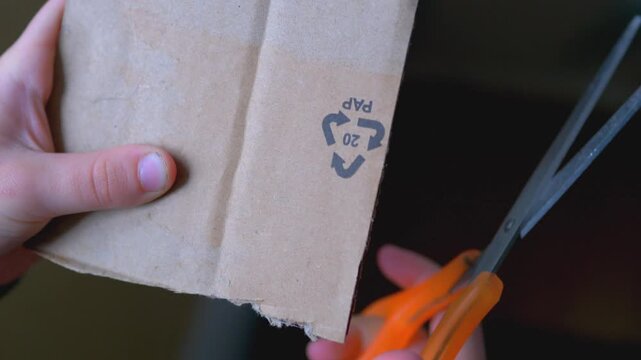 Close-Up of Cutting Brown Cardboard with Scissors, Recycling Symbol PAP 20 on Paper Packaging, Sustainable Waste Management and Eco-Friendly Disposal