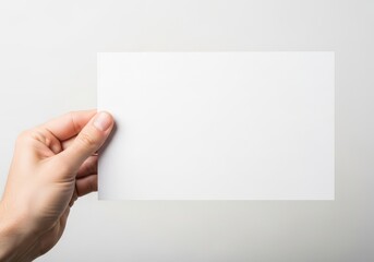 Obraz premium A hand holding a blank rectangular piece of white paper against a simple light gray background
