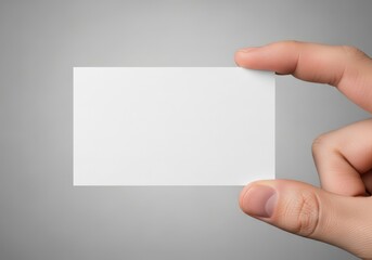 Obraz premium A hand holding a blank white business card against a soft gray background for design mockups