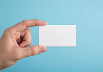 Obraz premium A hand holding a blank white business card against a plain light blue background for branding
